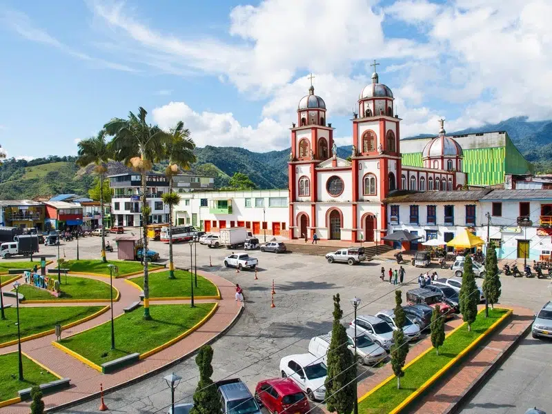 Plaza principal de Pueblo Rico, Risaralda, con su icónica iglesia de cúpulas rojas y blancas, rodeada de montañas y palmeras bajo un cielo despejado.