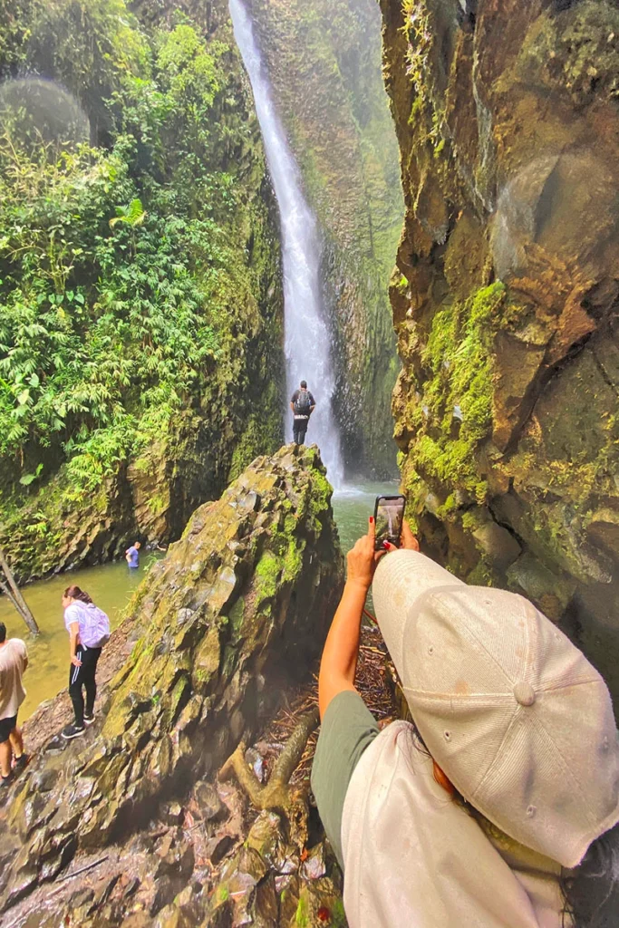 Caminante de espaldas con los brazos abiertos frente a una cascada en Risaralda, simbolizando la libertad y conexión con la naturaleza.