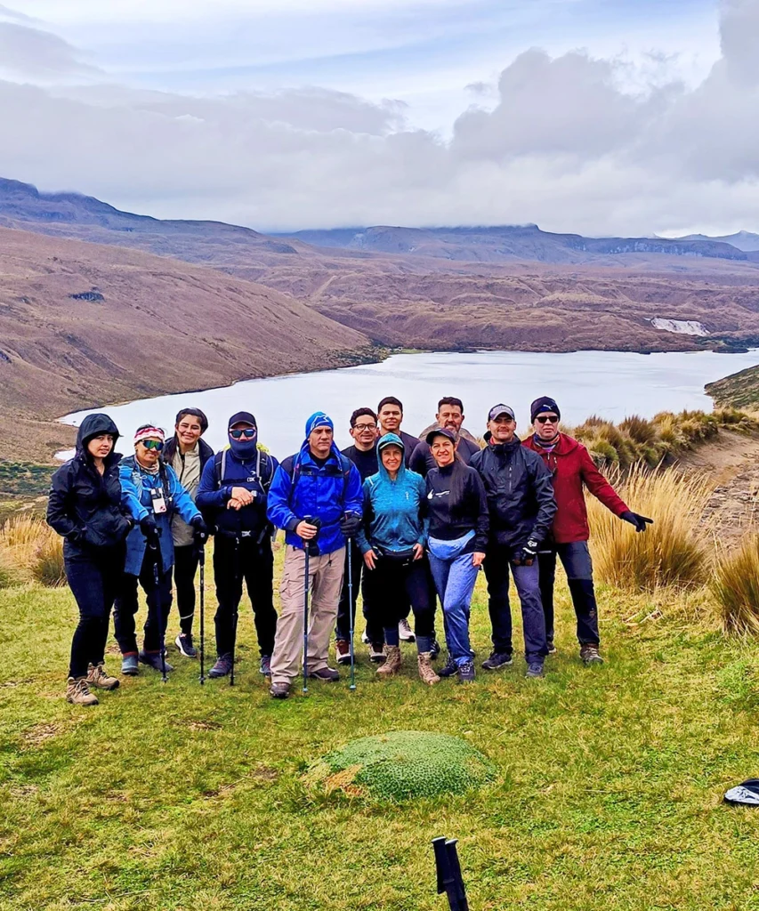 Grupo de montañistas con equipo técnico posando frente a una laguna encumbrada en el páramo de la Cordillera Central, Risaralda.