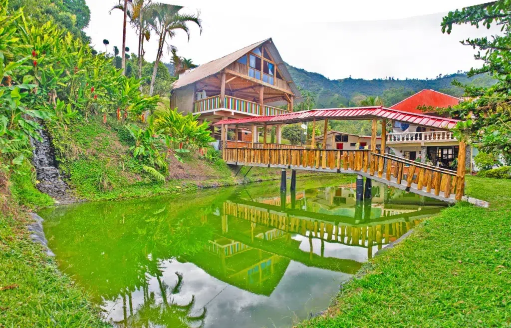 Vista panorámica del lago natural con puente de madera y la cabaña principal en Finca Los Arrendados.
